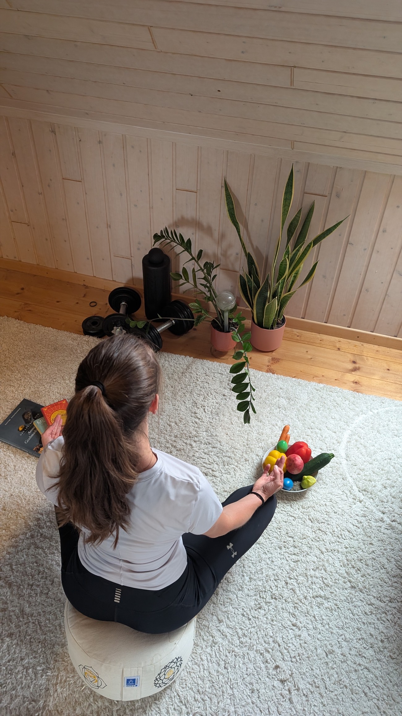 Frau meditiert im Schneidersitz auf einem Meditationskissen, daneben eine Schale mit Obst und Gemüse